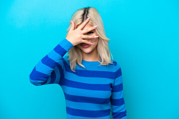 Young Russian woman isolated on blue background covering eyes by hands and smiling