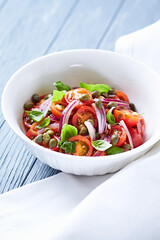 Simple salad with cherry tomatoes, red onion and fresh herbs. Bright wooden background. Close up.	