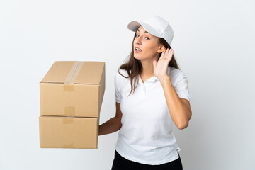 Young delivery woman over isolated white background listening to something by putting hand on the...