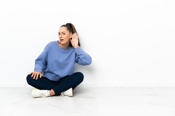 Young woman sitting on the floor listening to something by putting hand on the ear
