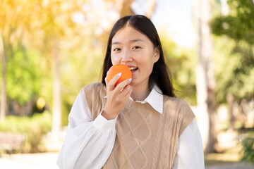 Fototapeta premium Pretty Chinese woman at outdoors holding an orange