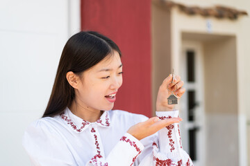 Young Chinese woman at outdoors holding home keys with surprised expression