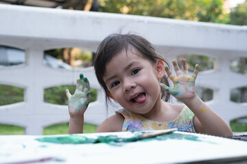 A joyful child shows off her painted hands while playing creatively outdoors.