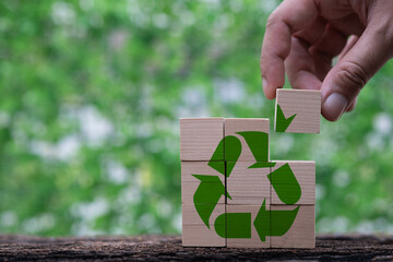 A hand is placing a block with a recycling symbol onto a stack of blocks, symbolizing sustainability and environmental awareness against a green background.