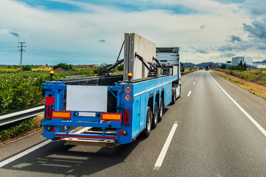 Fototapeta Truck driving on a highway with a specialized trailer for transporting precast concrete panels used in industrial building construction.Rear view.