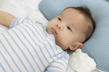
A baby is laying on a bed with a blue and white striped shirt. The baby has a serious expression on its face
