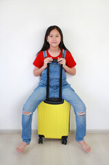 Portrait of Asian young girl sitting on suitcase posing and looking straight camera. kid fashion and travel concept.