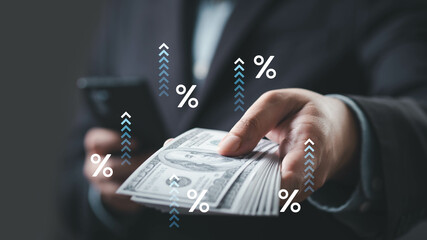 A person holding cash while using a smartphone, with percentage symbols and upward arrows indicating financial growth or interest.