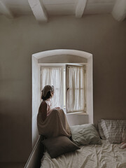 Woman Sitting by Window in Minimalist Bedroom