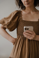 Close-Up of Woman Holding Smartphone in Brown Boho Dress, Neutral Background