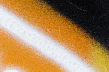 Macro close-up of a wall spray painted with orange, black and white with splashes. Abstract full frame textured splattered graffiti background with copy space.