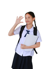Smiling Asian student girl in school uniform waving hand hello while carrying backpack bag and holding a book against white background.