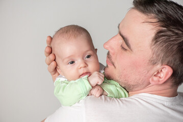 Handsome man father holding a cute smiling baby in his arms on a gray background