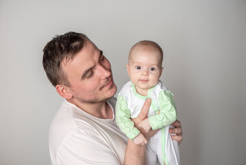 Handsome man father holding a cute smiling baby in his arms on a gray background
