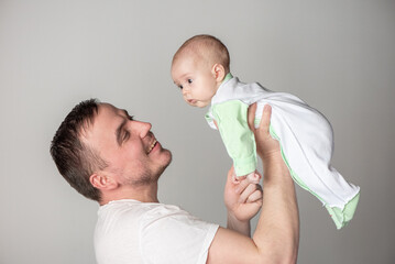 Handsome man father holding a cute smiling baby in his arms on a gray background