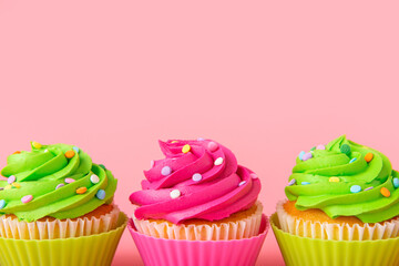 Three colorful cupcakes with bright icing and sprinkles on pink background