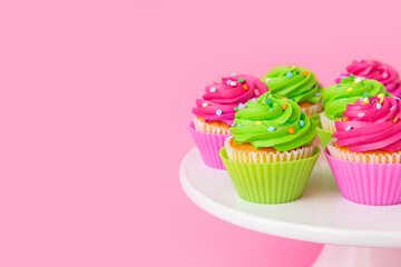 Colorful cupcakes with swirled frosting and sprinkles on pink background