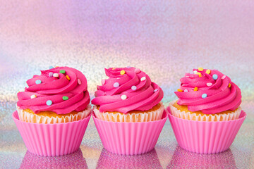 Three pink cupcakes on holographic background