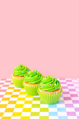 Green frosted cupcakes with colorful sprinkles on checkerboard and pink background