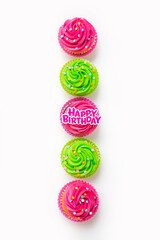Top view of colorful iced cupcakes arranged in row on white background with birthday topper
