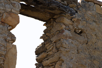 A close-up view of an opening in a crumbling stone wall, featuring an old wooden beam across the...