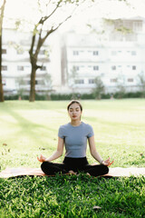 Fototapeta premium Young Asian woman practicing yoga outdoors on a sunny morning in a park, eyes closed, embracing calm, balance, and mindfulness.