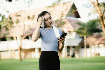Young Asian woman jogging in the sunny park, smiling and energetic, wearing activewear, enjoying...