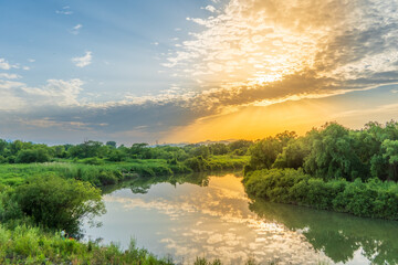 Golden sunset reflecting on a calm river winding through lush green vegetation © 佳灵 徐