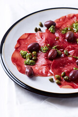 Slices of beef carpaccio with olives and capers. Close up.