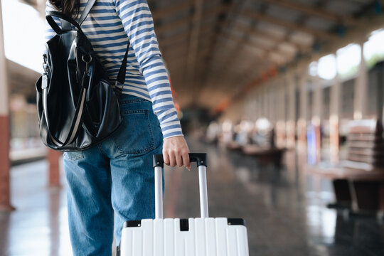 Stylish young woman traveling at train station with suitcase, traveling alone on vacation or business trip, enjoying summer city adventure.