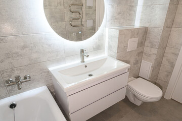 modern bathroom with gray tiles, white sink, illuminated mirror, and toilet. Clean and minimalist...