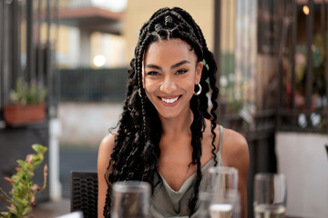 Portrait of a happy young beautiful woman with braids smiling at camera at an outdoor cafe.
