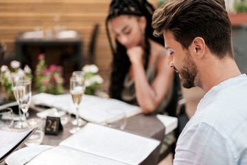 Couple on a romantic date at an outdoor restaurant, reading the menu to choose food and wine.