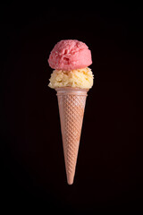 Strawberry and vanilla ice cream cone with two scoops, isolated on a dark black background.