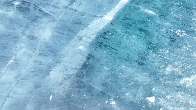 Close up view of cracked crystal blue ice surface. Frozen water texture and pattern of natural ice. Winter nature background footage.