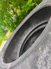 A tire with a hole in it is shown in a forest. The tire is black and has a hole in the middle. The tire is surrounded by trees and bushes, giving the image a natural and peaceful feel