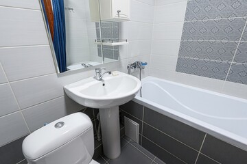 clean bathroom with white & gray tiles, a toilet, sink, tub, and heated towel rack