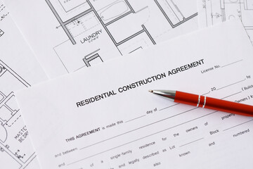 Pen on residential construction agreement and planning blueprints of residential building project close up. Construction plan concept
