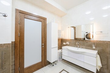 Well-lit bathroom with modern white fixtures, a wooden-framed door, and neutral tile. The space is clean and functional