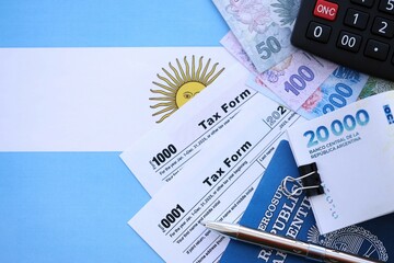 Argentine pesos money bills in big amount lies on table with pen, calculator, passport and tax forms