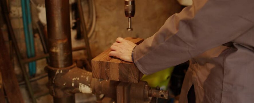 Falegname posiziona pezzo di legno sotto trapano verticale a colonna per forarlo