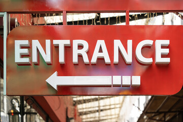 The image shows a red entrance sign with the word "ENTRANCE" in bold white letters and a white left-pointing arrow below it.