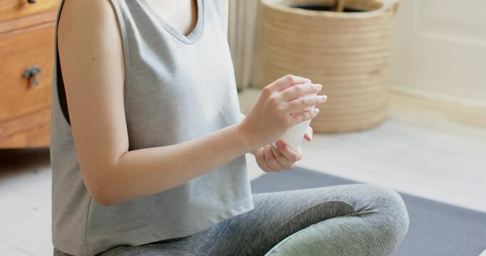 Asian woman finishing workout, taking supplements with water, checking smartwatch in living room