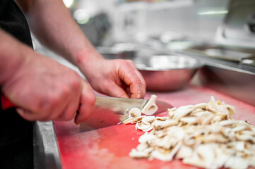 A person slices fresh mushrooms on a red cutting board in a kitchen. The scene highlights food preparation with a knife, showcasing precision and culinary skills.