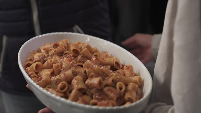 detail of a white ceramic tray with a large portion of pasta with tomato sauce held in the hand of a person