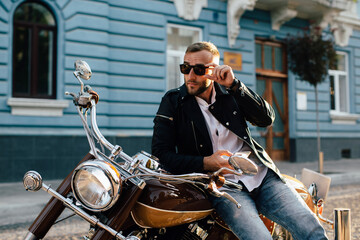 Stylish motorcyclist adjusting sunglasses while sitting on motorbike