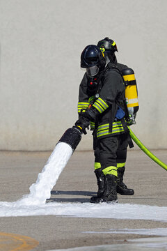 Firefighter with Protective Mask and Oxygen Bottle while operating lance spraying white foam