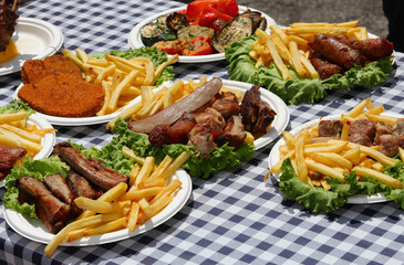table with white and blue checkered tablecloth and many plates full of meat and fries