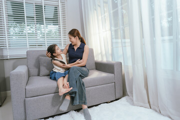Obraz premium An Asian mother and daughter sit together indoors, smiling and bonding over a book, enjoying digital learning and joyful family time.