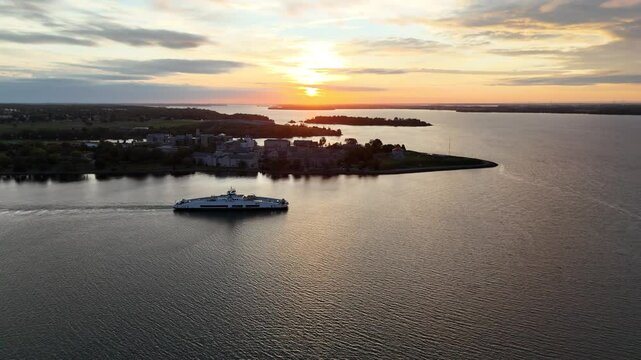 Aerial scene of Wolfe Island Ferry IV sails at sunrise in fall with RMC Kingston in the background